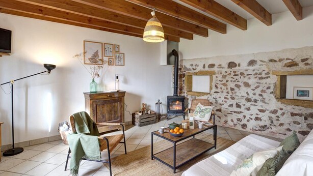 A cozy living room with exposed wooden beams, a stone wall, a fireplace, a sofa, a coffee table, and a lamp.