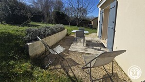 A patio with two chairs and a table, a concrete planter, and a building with a garage door. - Cozy House in Périgord Noir with Garden (Cénac-et-Saint-Julien)