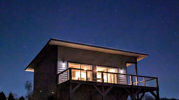 Una cabaña de dos pisos con un balcón, rodeada por un paisaje natural de noche.