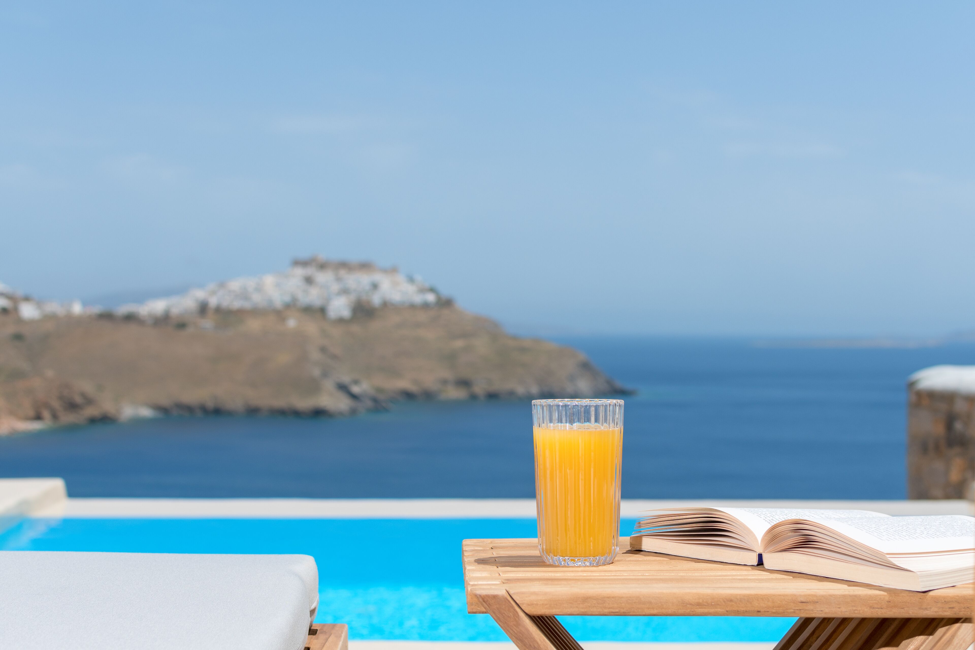 A poolside setting with a clear view of the sea and a rocky outcrop in the background.