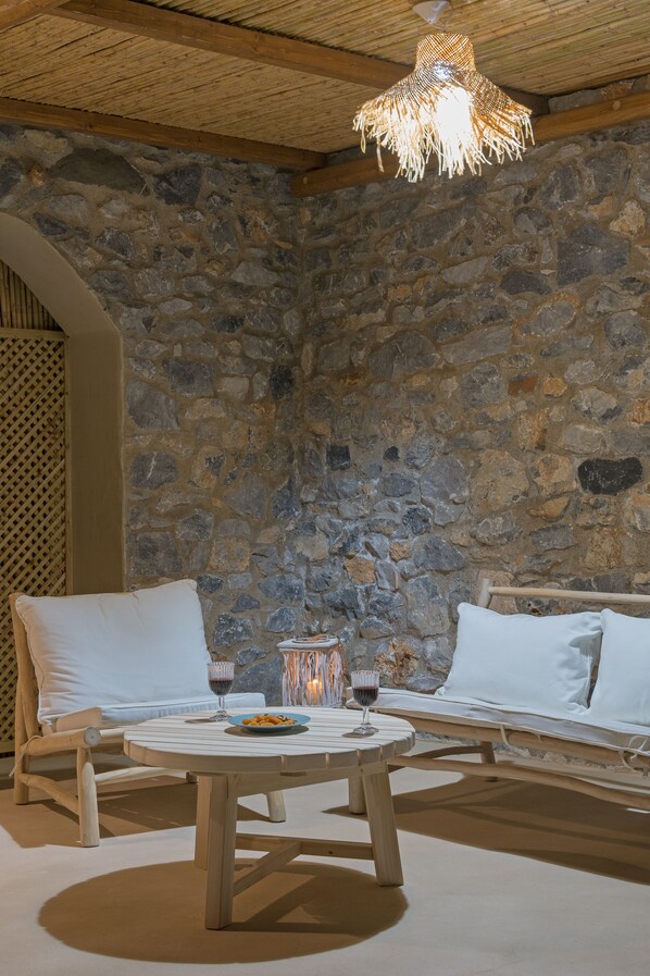 Una habitación con paredes de piedra, una mesa redonda de madera, dos sofás blancos acolchados y una lámpara colgante.