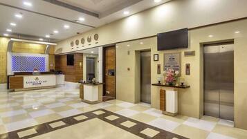 A hotel reception area with a check-in counter, reception desk, and a reception area with a flat-screen TV mounted on the wall.