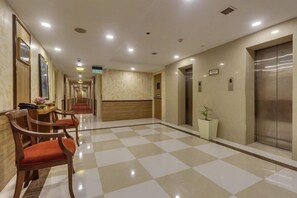 Eine Hotelhalle mit Schachbrettmuster-Boden, Holzsesseln, einem Aufzug und einer Rezeption.