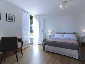Un dormitorio con cama, escritorio, silla y puerta que da al exterior.