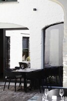 An outdoor dining area with a white brick wall, black metal chairs, and tables set for dining.
