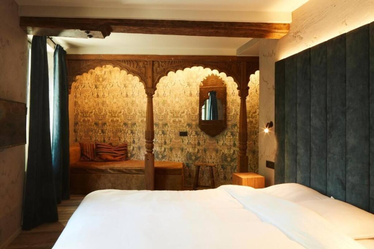 A bedroom with a large bed, a wooden bench, and a stone wall with carved patterns.