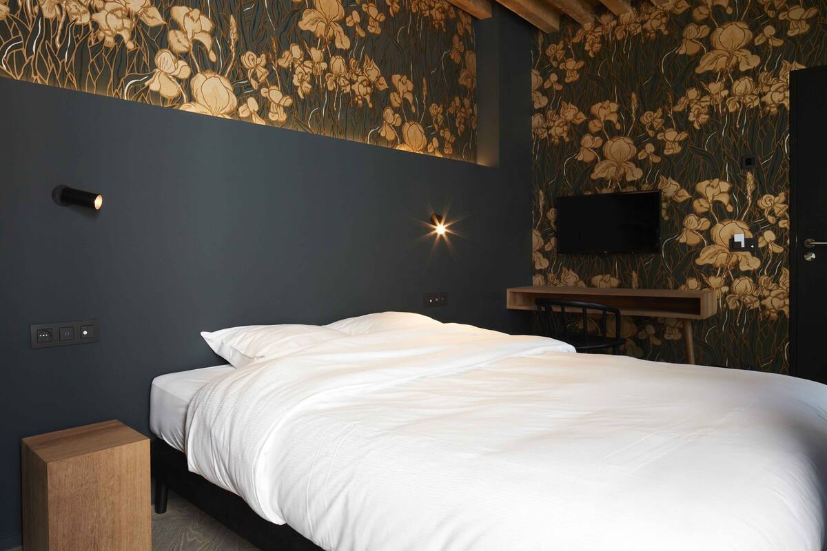 A bedroom with a bed, a TV mounted on the wall, and a wooden nightstand.