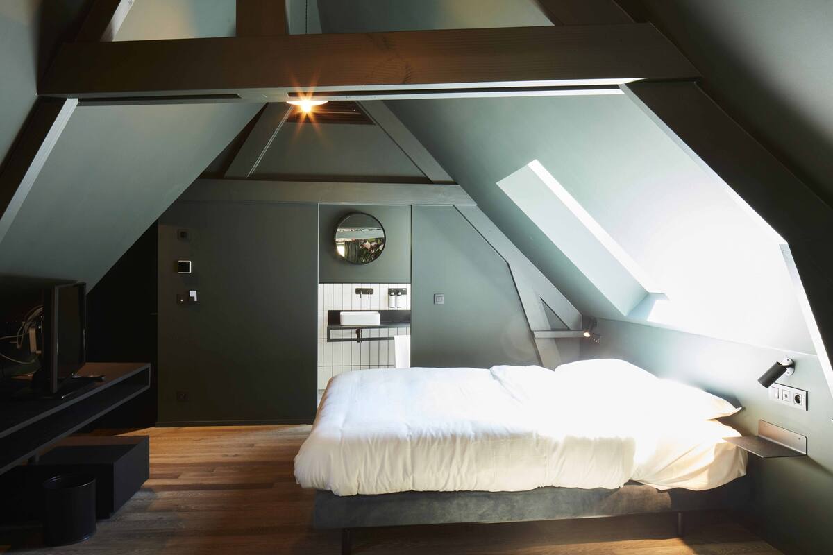 A compact, modern loft bedroom with a skylight, a built-in desk, and a small kitchenette.