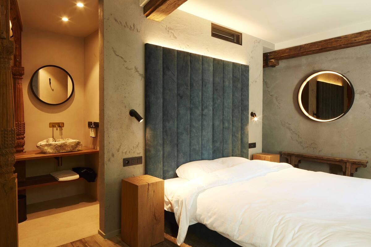 A bedroom with a bed, a round mirror, a wooden nightstand, a built-in shelf, and a wall-mounted heater.