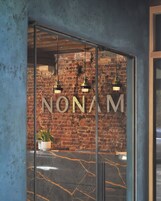 A modern interior with a brick wall, a glass door with the inscription "NONAM", and hanging pendant lights.
