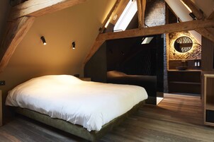 A bedroom with a large bed, wooden beams, a skylight, and a stone wall with a circular window.