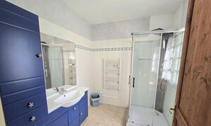 A bathroom with a blue vanity, a white sink, a glass shower enclosure, and a towel rack.