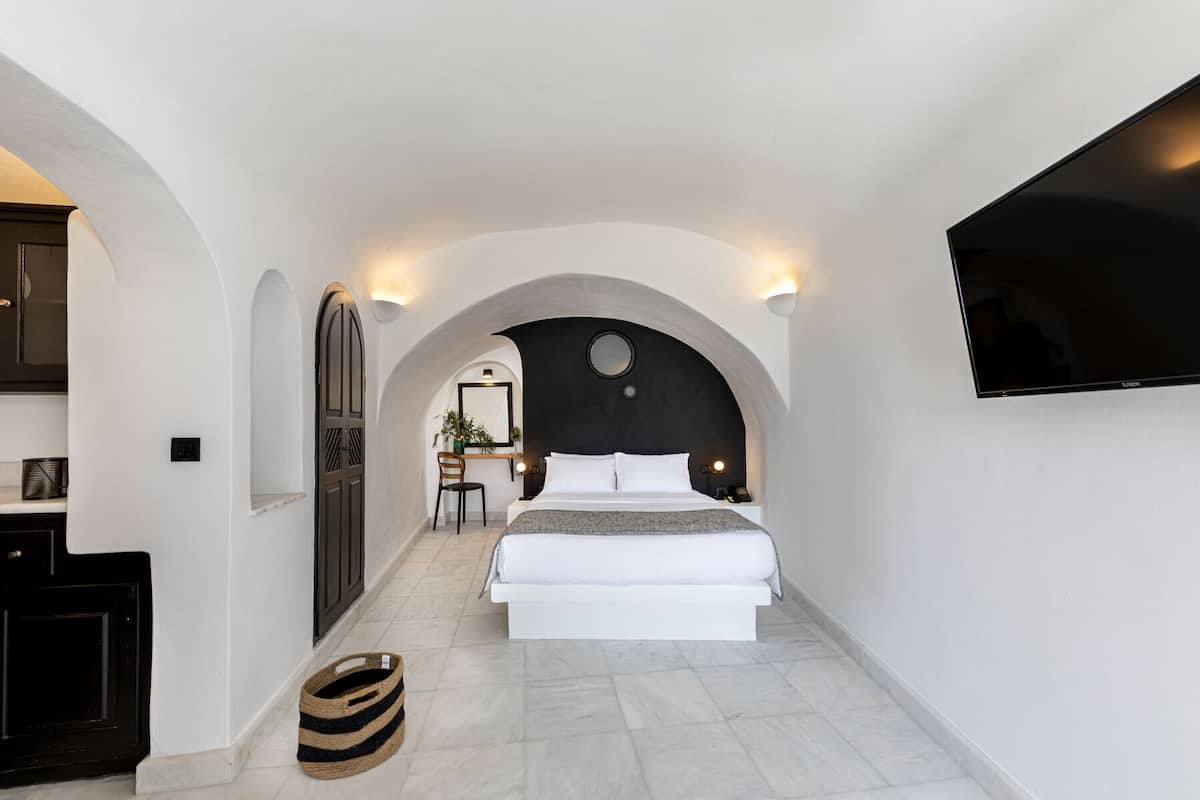 A modern bedroom with a large bed, a desk, and a TV mounted on the wall.