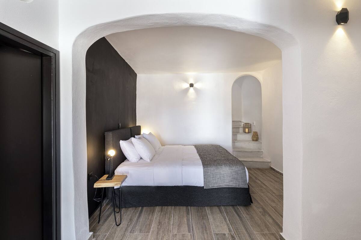 A modern bedroom with a dark headboard, a wooden side table, and a bed with white bedding.