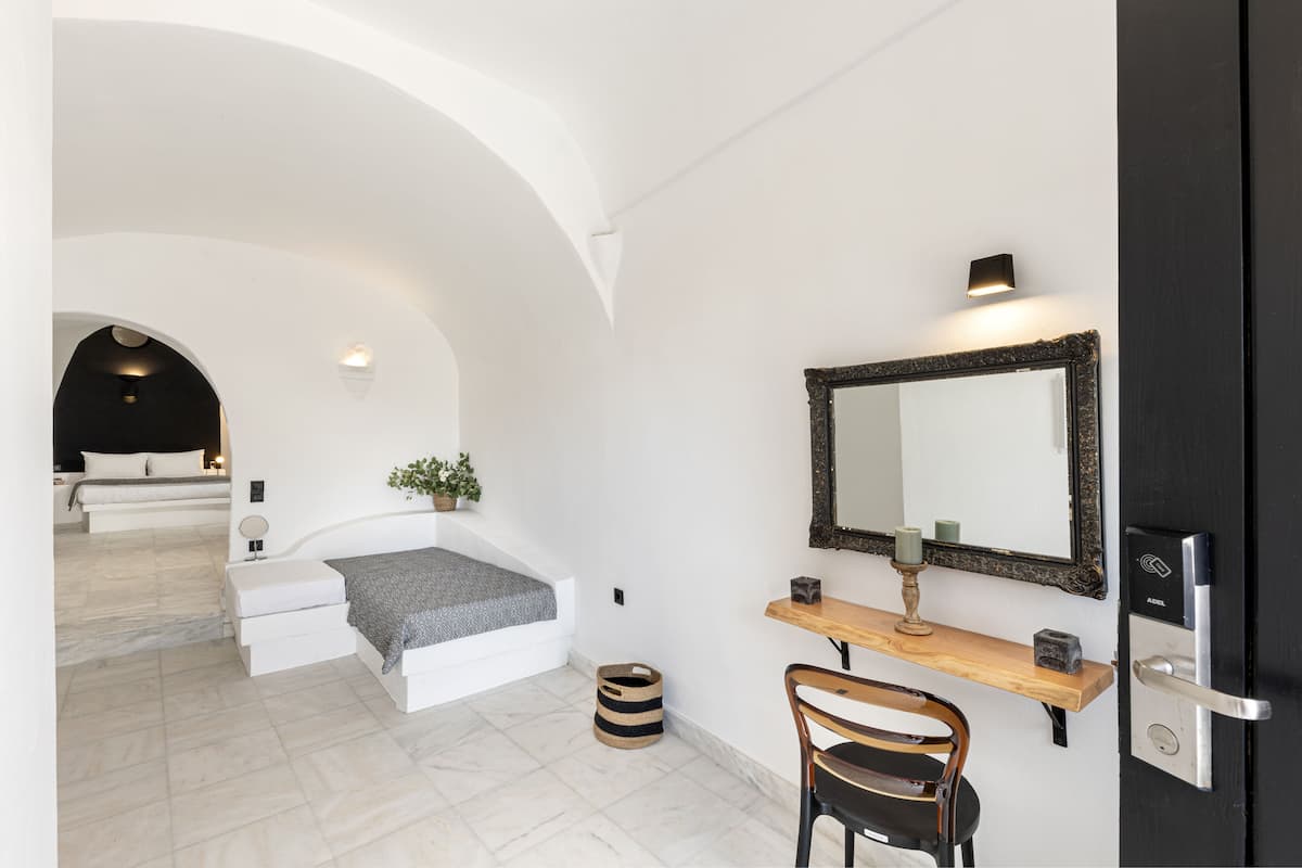 A modern bedroom with a white bed, a bedside table, a mirror, and a door with a key lock.