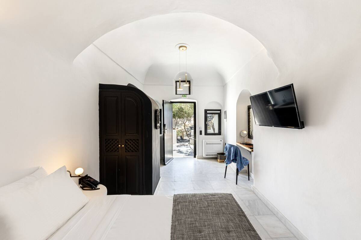 A hallway with a bed, a desk, a TV, and an open door leading to a balcony.