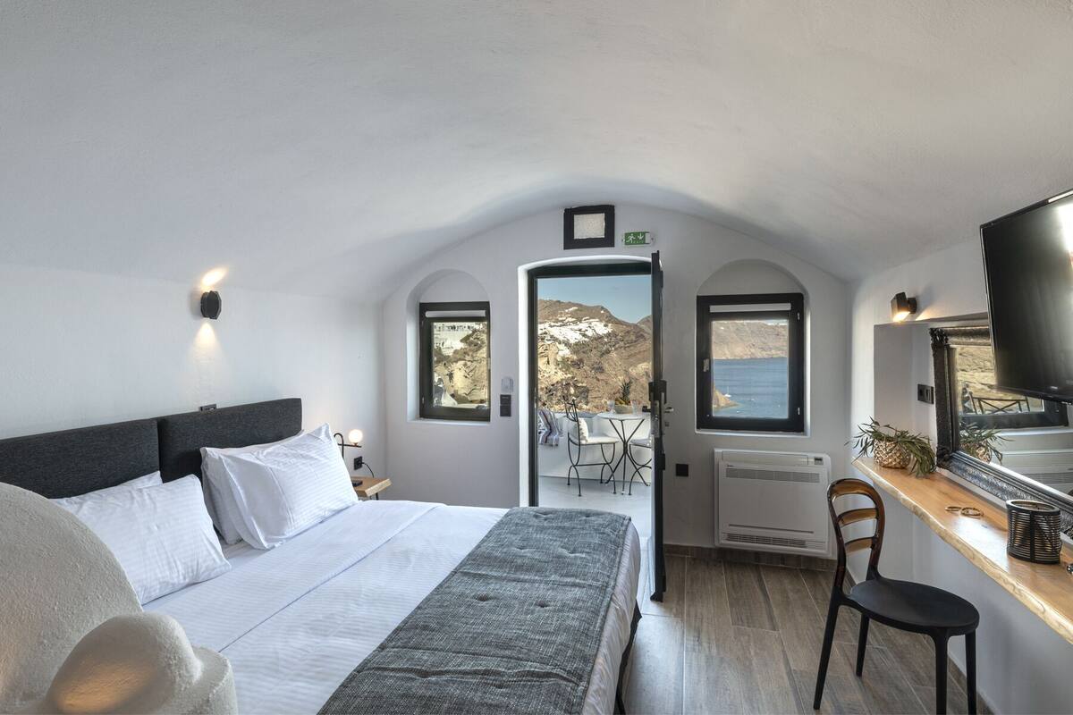 A bedroom with a bed, a desk, a chair, and a TV. There are windows with views of the outside.