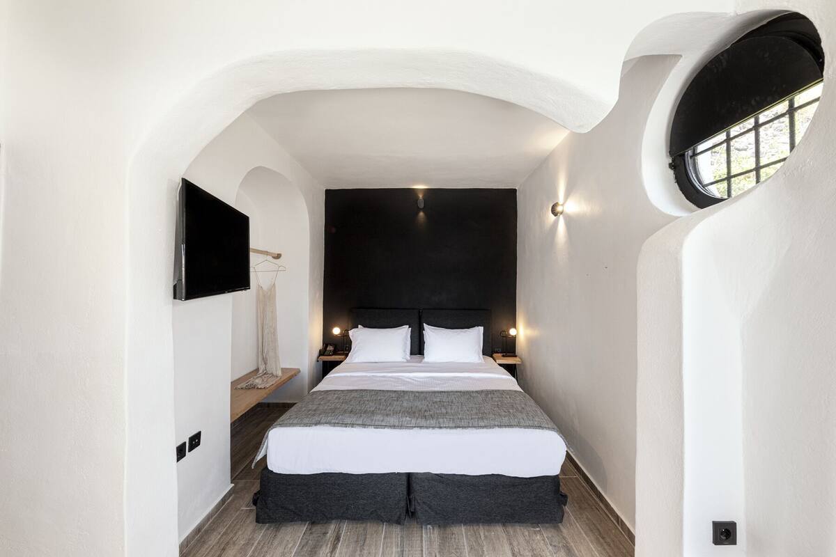 A modern bedroom with a large bed, a TV mounted on the wall, and a small bedside table.