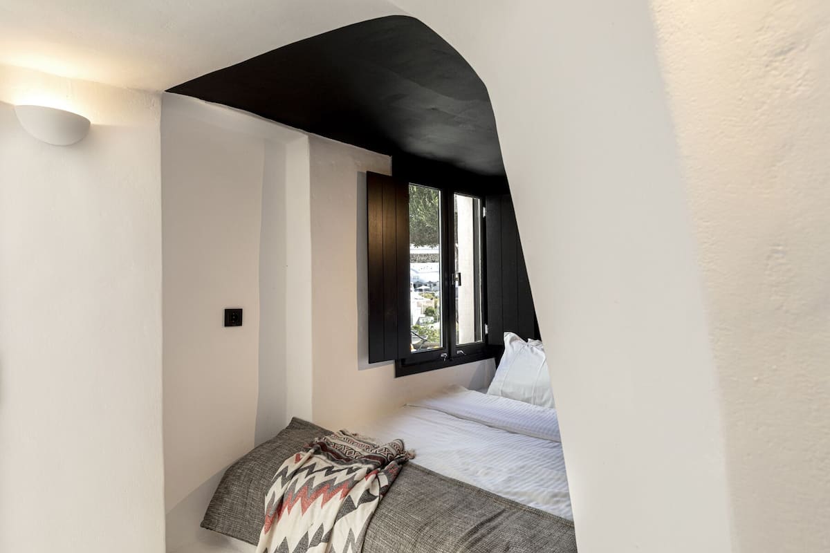 A bedroom with a sloped ceiling, a bed with white bedding, a patterned throw blanket, and a window with a view of the outside.