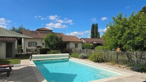 A swimming pool with a tiled deck, surrounded by a wooden fence, and houses with tiled roofs in the background. - Birdsong: Private Pool, Wifi, Pets Welcome, Garden (Chancelade)