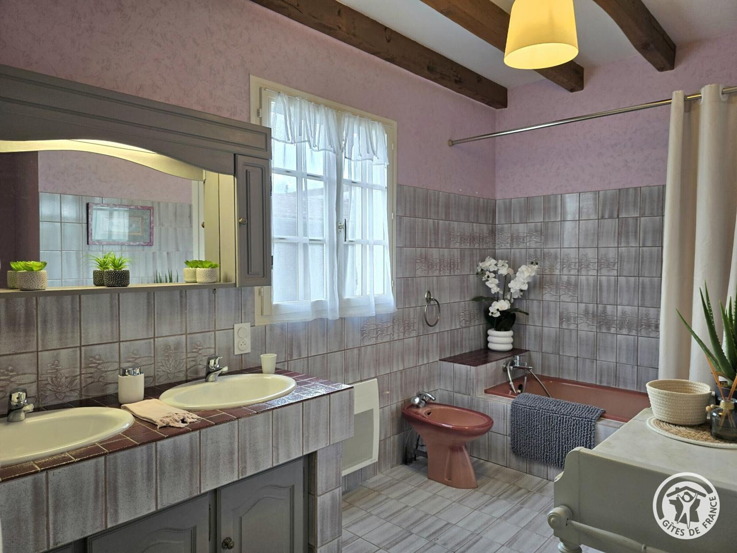 A bathroom with two sinks, a bidet, a mirror, and a window with curtains.