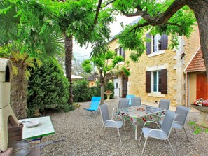 An outdoor patio with a table and chairs, surrounded by trees and a stone building. - Holiday home in Dordogne with shared pool and pets allowed (Calviac-en-Périgord)
