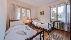 Ett hotellrum med två separata sängar, en sänggavel i trä, ett nattduksbord med en lampa, ett element och ett fönster med gardiner.