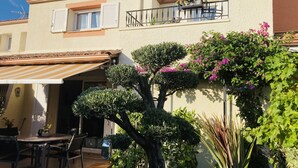 A residential building with a patio area featuring a table and chairs, surrounded by well-maintained shrubs and flowering plants. - SUPERB VILLA 80 m2 in DUPLEX, 6 pers, 3 bedrooms, 2 bathrooms + garage and garden (Agde)