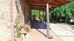 A covered patio area with stone flooring, wooden furniture, and potted plants. - Townhome (Cefalù)