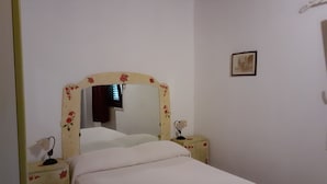 A bedroom with a single bed, a bedside table with a lamp, a mirror with floral design, and a small framed picture on the wall. - Townhome (Cefalù)