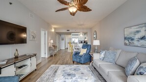 A modern living room with a ceiling fan, a flat-screen TV, a sofa, and a coffee table. - Ariel Dunes I 508 * Beachy* Modern* 3 pools* (Miramar Beach)