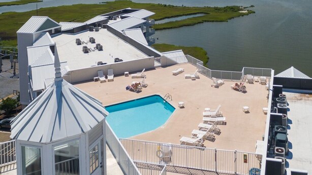 A rooftop pool area with lounge chairs and a swimming pool, overlooking a body of water and a distant island.