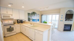 A modern kitchen with white cabinets, a microwave, stove, and dishwasher. There is a large window with a view of the ocean.