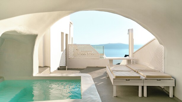 A white, arched room with a view of the sea, a pool, and two white lounge chairs. - Anemos Cave Suites (Santorini)