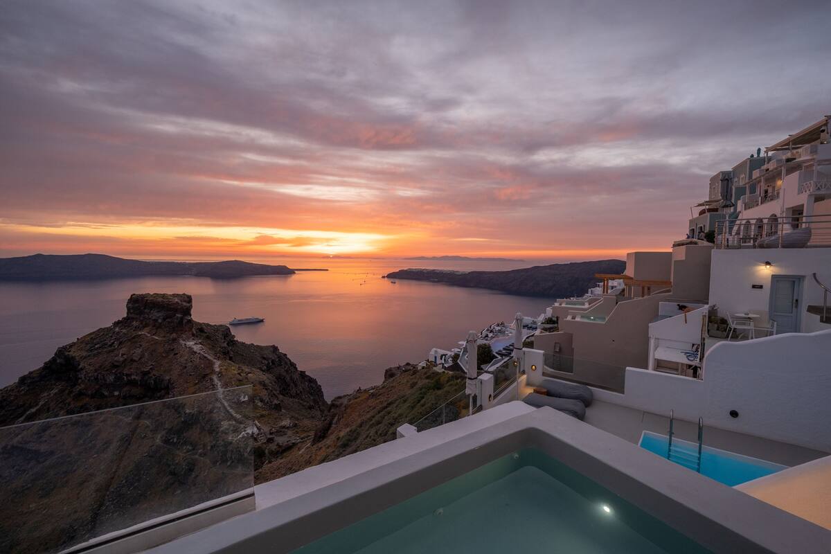 Vista del atardecer desde el balcón de un hotel con vista al mar tranquilo y a una costa rocosa.