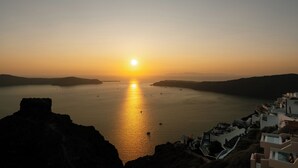 Vista de um pôr do sol costeiro com céu claro, mar calmo e um edifício branco com varandas voltadas para a água.