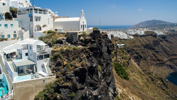 Uma vila costeira com edifícios brancos, um penhasco rochoso e vista para o mar.