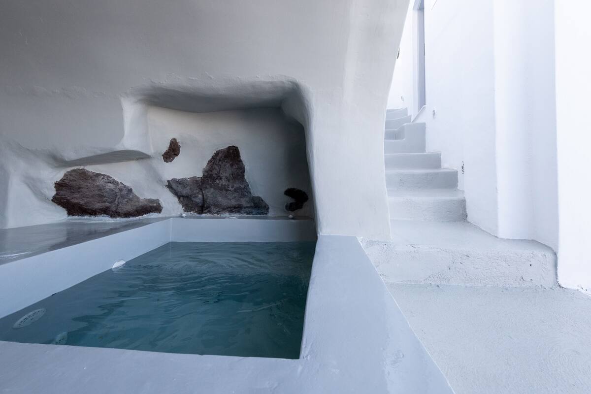 Una piscina infinita blanca con vista al mar, rodeada de muros blancos y una escalera.