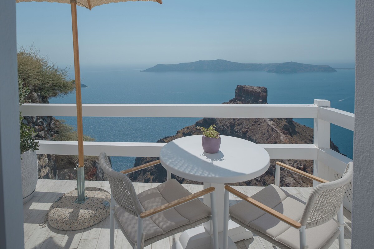 A balcony with a round table, two chairs, a woven umbrella, and a potted plant.
