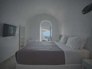 Un dormitorio moderno con una cama grande, un televisor montado en la pared y vistas al exterior a través de un arco.