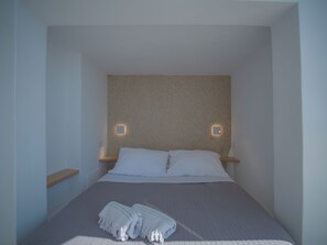 A bedroom with a bed, two bedside tables, and two wall-mounted light fixtures. - Anemos Cave Suites (Santorini)