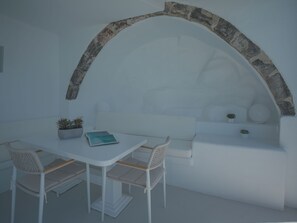 Un interior en blanco con un arco de piedra, un sofá blanco, una mesita con un libro y dos sillas.