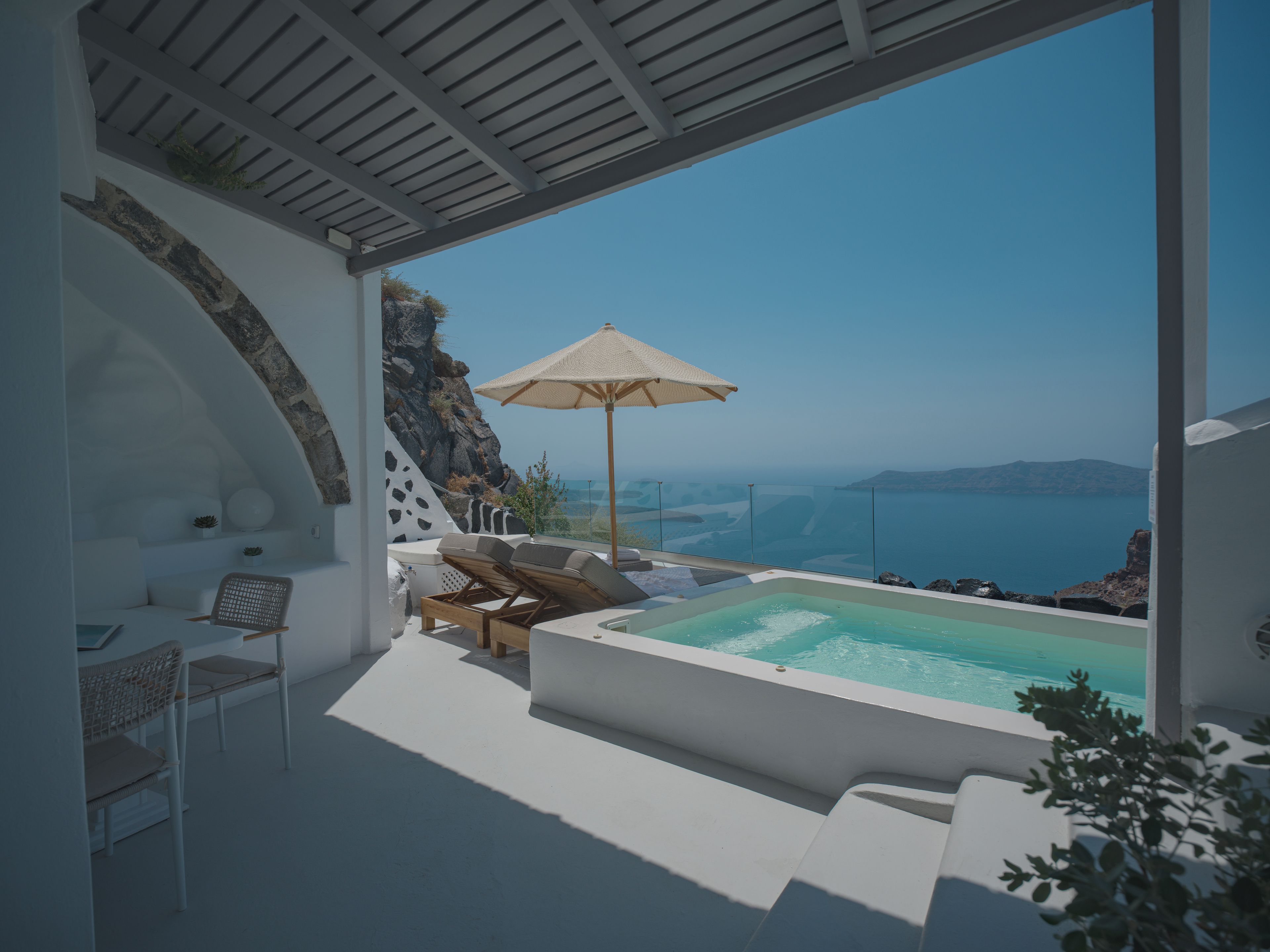 A modern outdoor lounge area with a pool, seating, and a view of the sea.