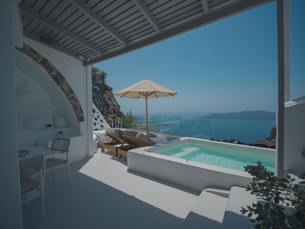 A modern outdoor lounge area with a pool, seating, and a view of the sea. - Anemos Cave Suites (Santorini)