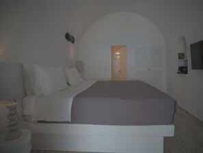 Un dormitorio con cama, mesita de noche y puerta que da a otra habitación.