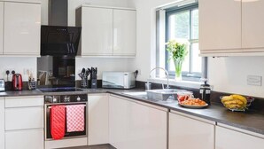 A modern kitchen with white cabinets, a black microwave, a red kettle, and a window with a view of greenery. - Stylish 3-bed Cottage Located in the Cairngorms (Ballindalloch)