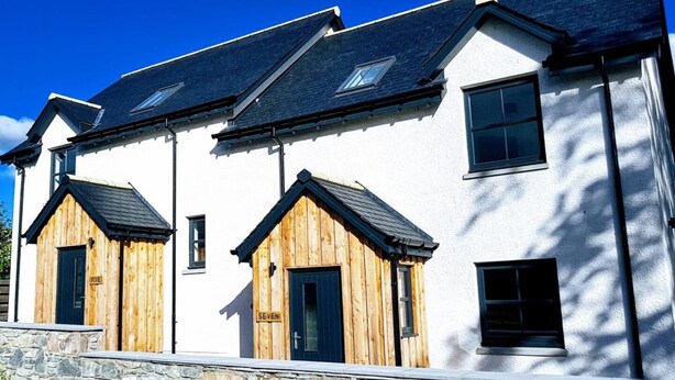 A row of white buildings with black roofs and wooden doors labeled "FIVE" and "SEVEN". - Stylish 3-bed Cottage Located in the Cairngorms (Ballindalloch)