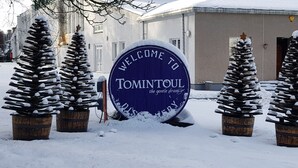 A snow-covered welcome sign for Tomintoul, surrounded by snow-laden pine trees. - Stylish 3-bed Cottage Located in the Cairngorms (Ballindalloch)
