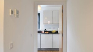 A hallway leading to a kitchen with white cabinets, a black countertop, and a wooden floor. - Stylish 3-bed Cottage Located in the Cairngorms (Ballindalloch)