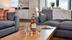 A modern living room with grey sofas, a wooden coffee table, and a bottle of Tomintoul 16 single malt Scotch whisky. - Stylish 3-bed Cottage Located in the Cairngorms (Ballindalloch)
